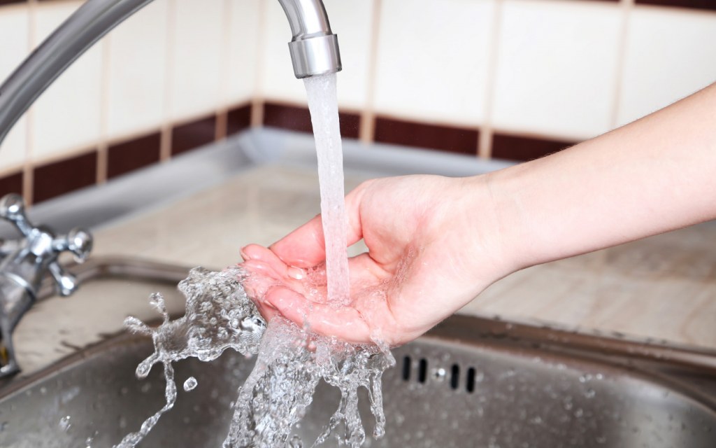 Woman washes hand running water kitchen faucet
