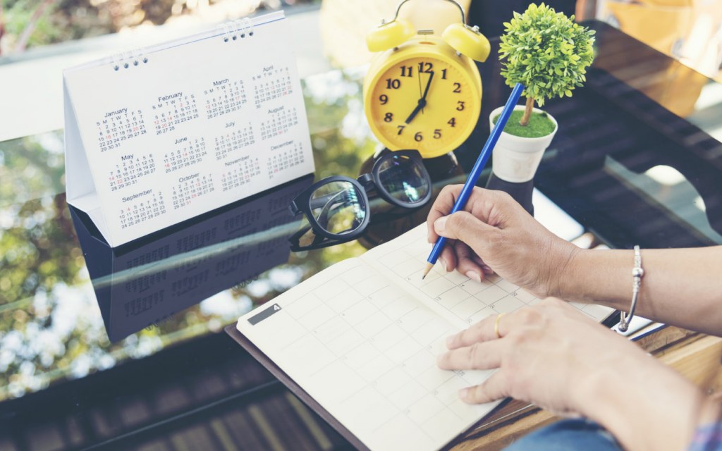 Woman writing in a schedule planner next to a calendar and a clock