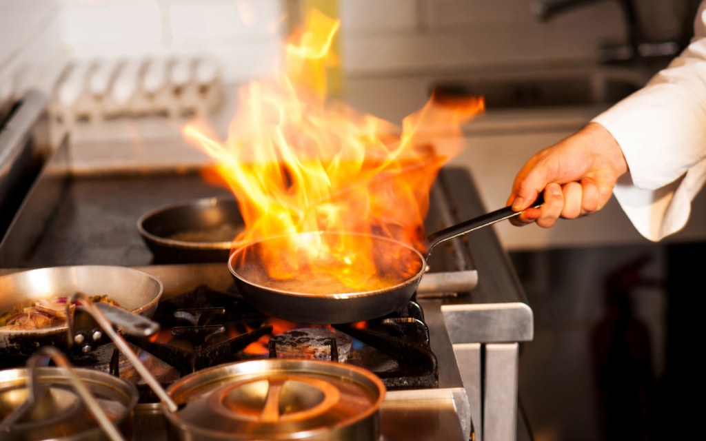 Chef cooks with flame in a frying pan on a gas stove