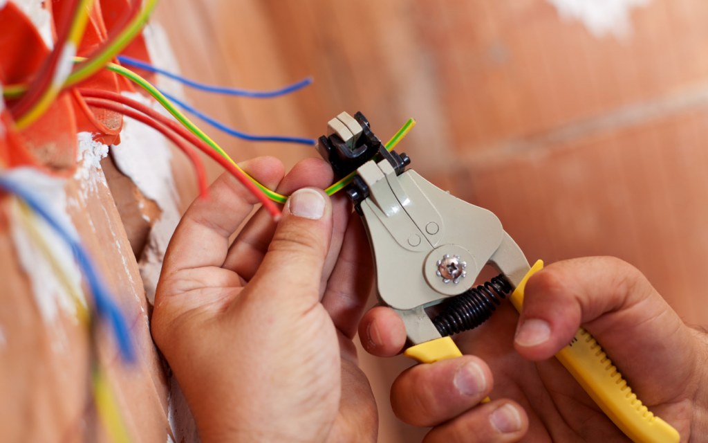 Electrician using pliers to peel off insulation from wires