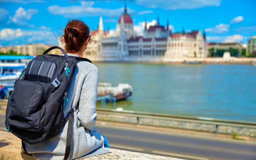 Traveler with backpack sits at bank of river Danube in Budapest