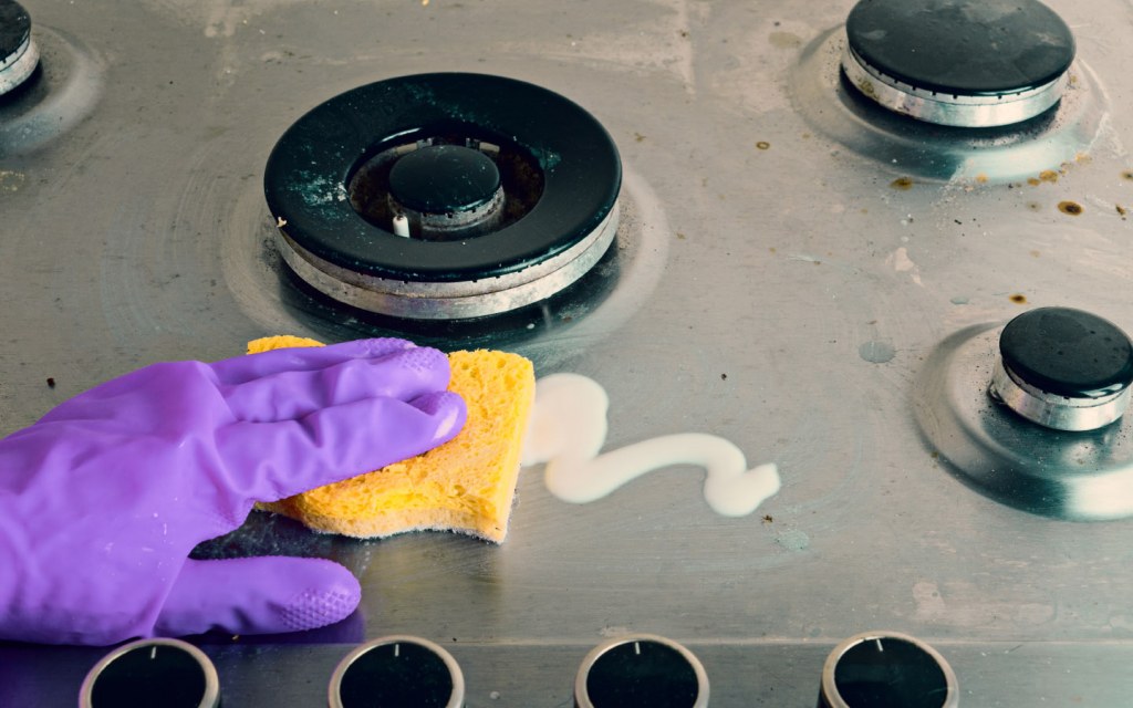 Person scrubbing cleaning stove top with a sponge
